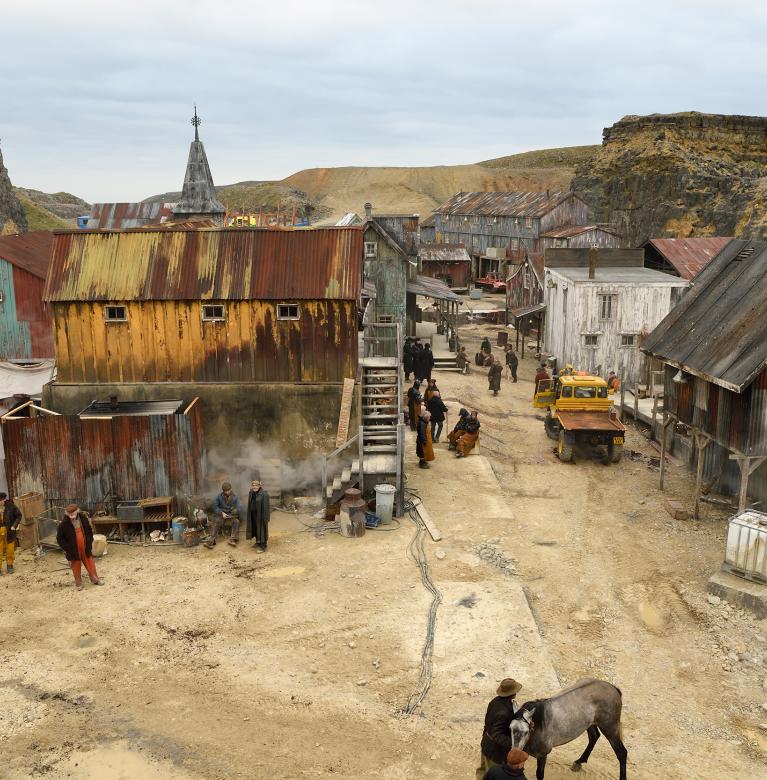 Filming location depicting a town set with metal houses and huts against a quarry backdrop