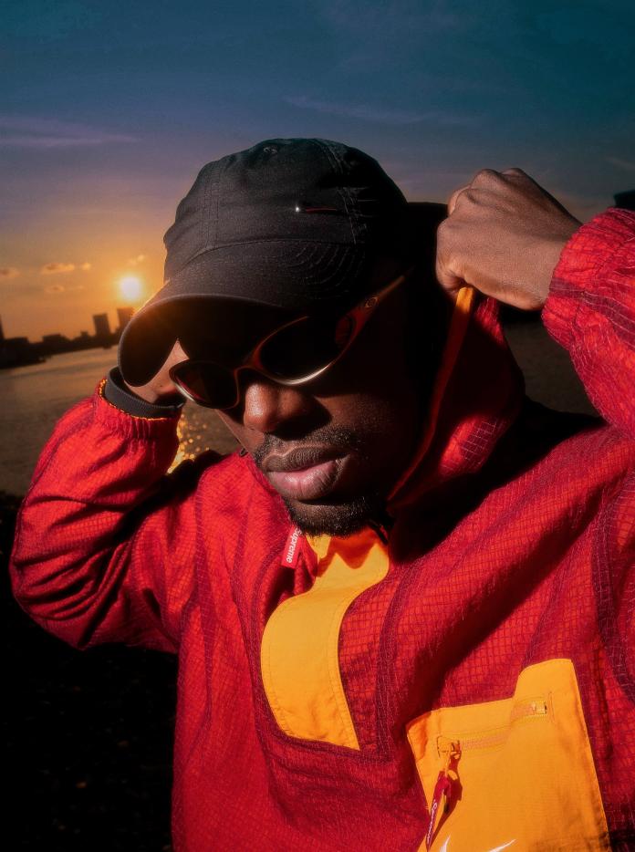 a close up of artist Lemfreck's face, wearing sunglasses and a black cap and red hoodie