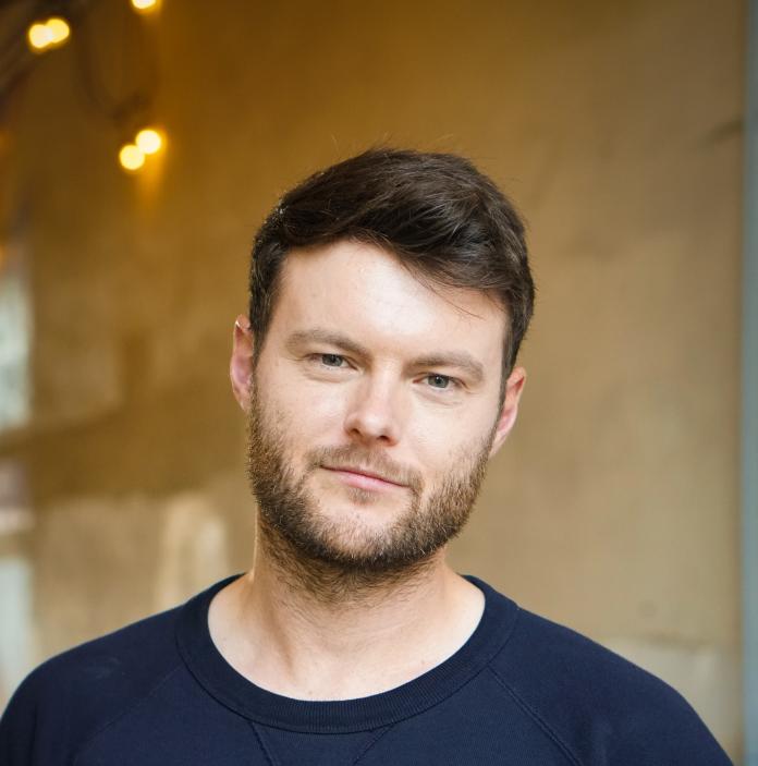 headshot of man with brown hair and blue jumper