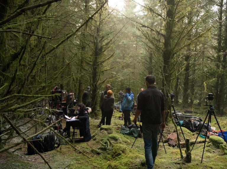 Group of people gathering in forest location with tall green trees and mossy green floors to film