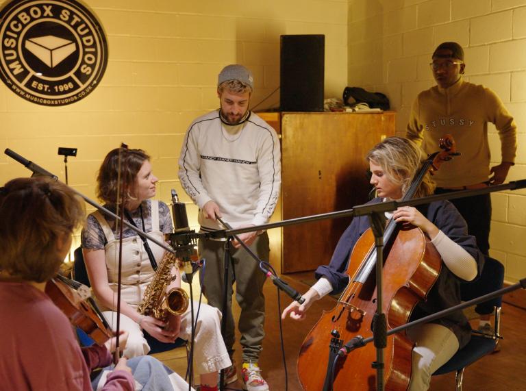Three musicians sitting together to play – including a saxophone player and a cello player