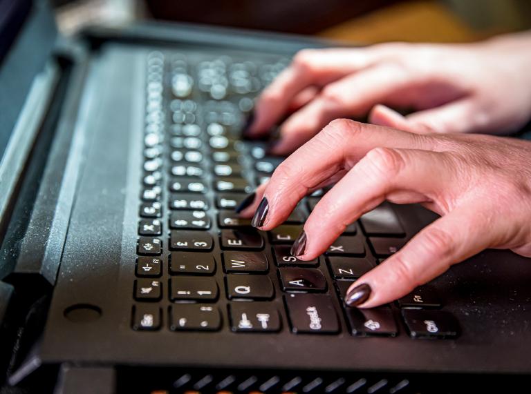 Close up of hands typing on a black pc keyboard.