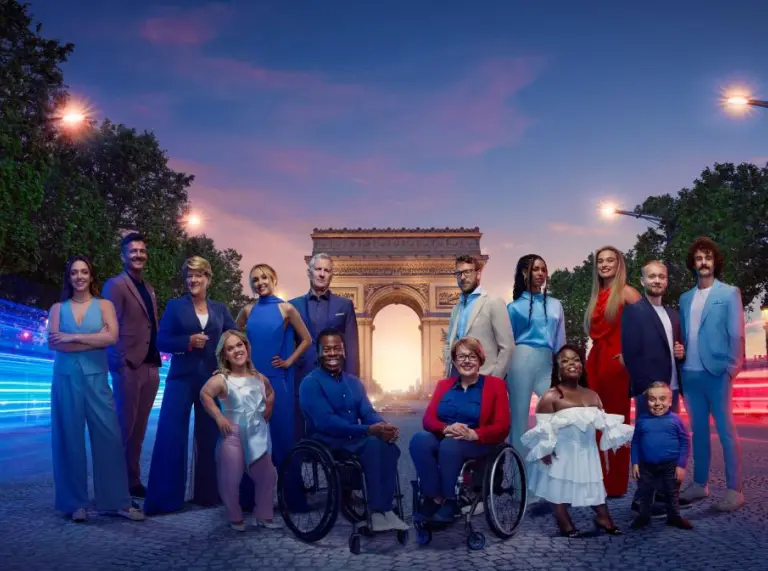 Diverse group of individuals posing together on a Parisian street with the Arc de Triomphe in the background at dusk