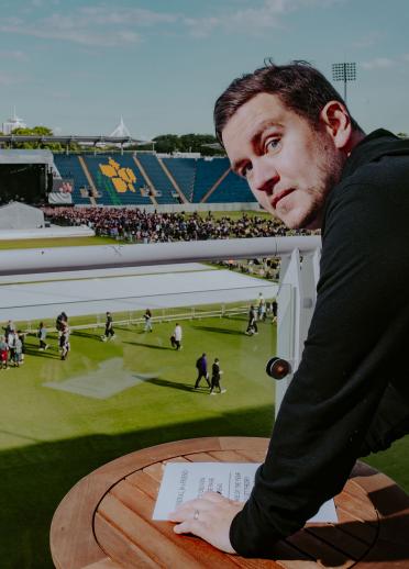 Medium shot of Ryan Richards, who's wearing a black jacket, standing in front of a crowd at the Swalec Stadium in Cardiff.