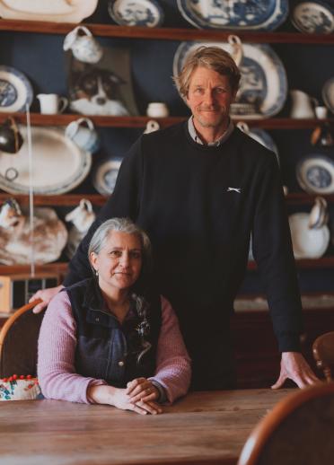 A woman sitting at a dining table as a younger man stands over her shoulder as they smile