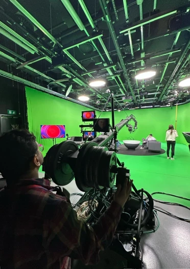 Television studio with a green screen, camera equipment, and crew preparing for production