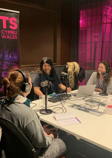 People recording a podcast around a table with microphones and equipment in a studio setting