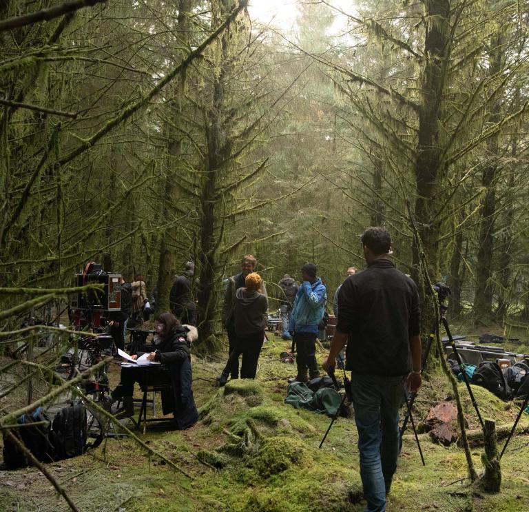Group of people gathering in forest location with tall green trees and mossy green floors to film