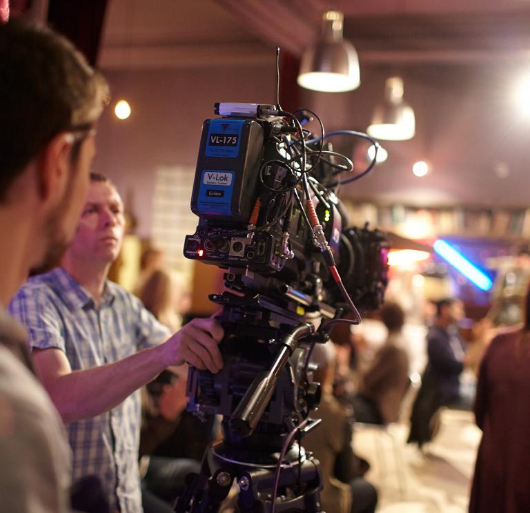 Over the shoulder shot of a person operating a big TV camera in a studio