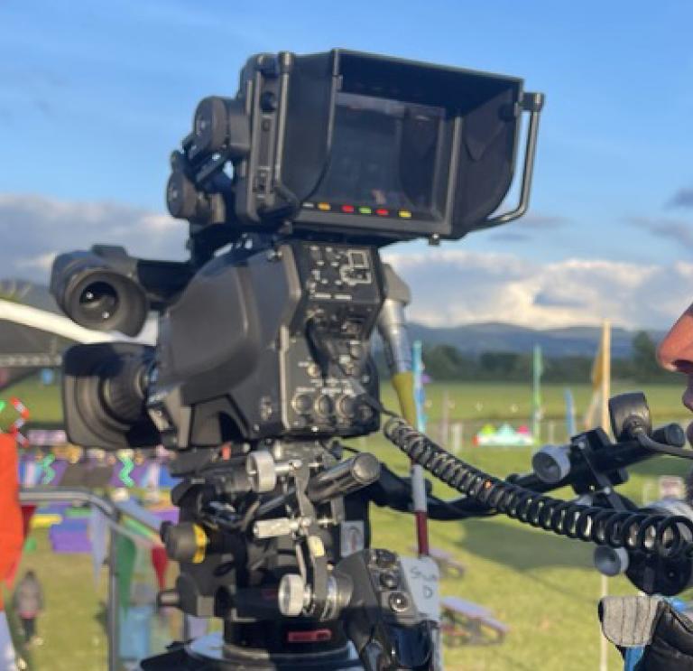 Close up shot of person wearing headphones operating a film camera on location in countryside.  