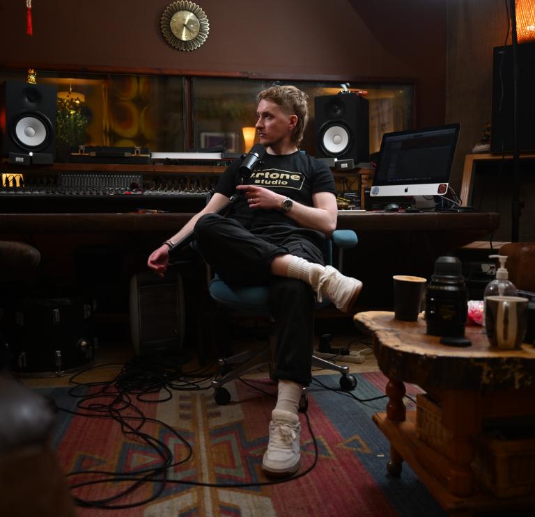 white man sits in recording studio with equipment in the background