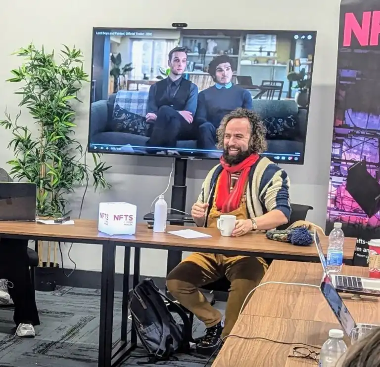 Workshop discussion at NFTS Cymru Wales with participants seated at a table, a presentation screen, and promotional banner in view