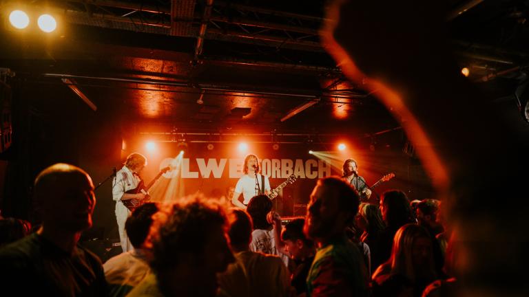 A busy crowd under red lights at a Buzzard Buzzard Buzzard gig at Clwb Ifor Bach