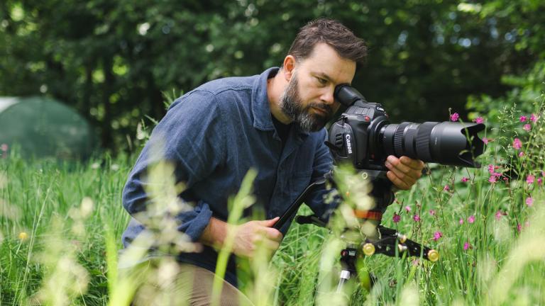 Close up shot of a person wearing a blue coloured shirt looking through a camera lens.