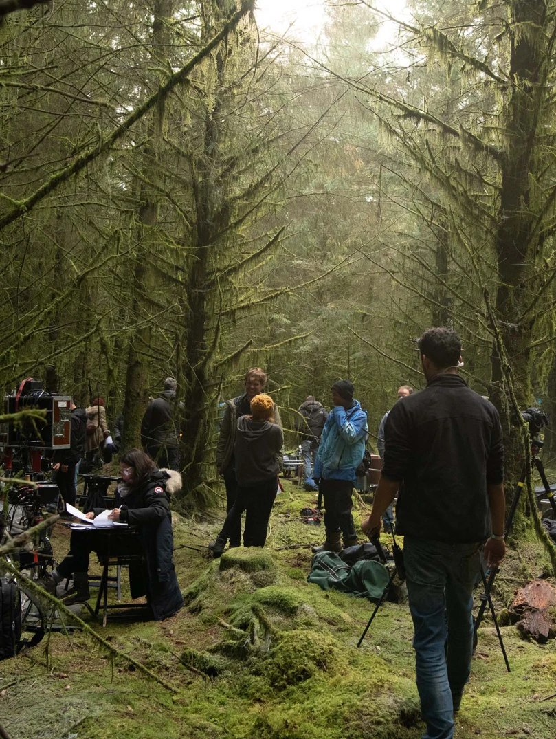 Group of people gathering in forest location with tall green trees and mossy green floors to film