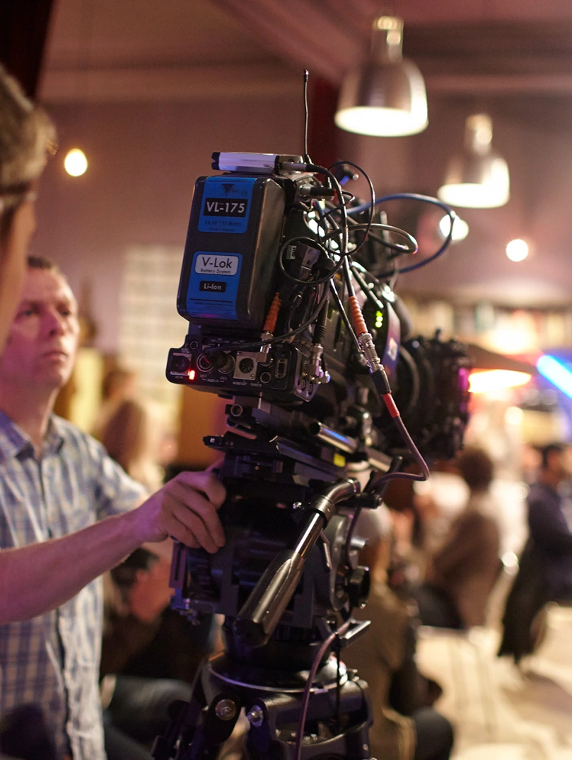 Over the shoulder shot of a person operating a big TV camera in a studio