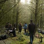Group of people gathering in forest location with tall green trees and mossy green floors to film