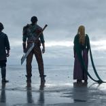 Four people stand on the end of the shore looking out to sea