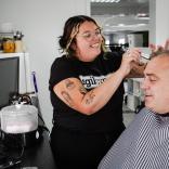 Trainee Fiorella Wyn, smiles as she is doing make up on a male participant back stage