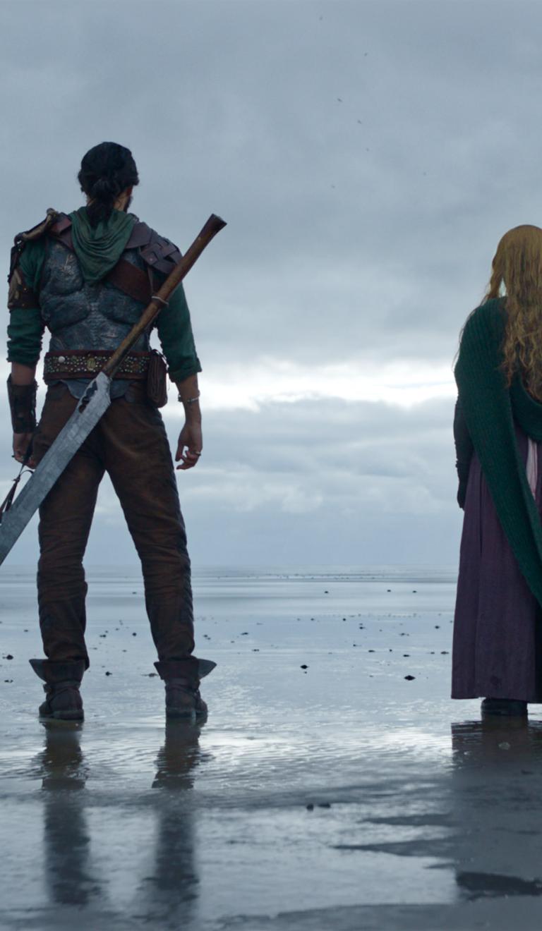 Four people stand on the end of the shore looking out to sea