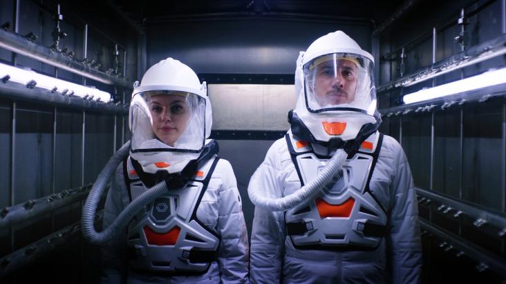 A screenshot of two people wearing white scientist suits from The Complex by Wales Interactive