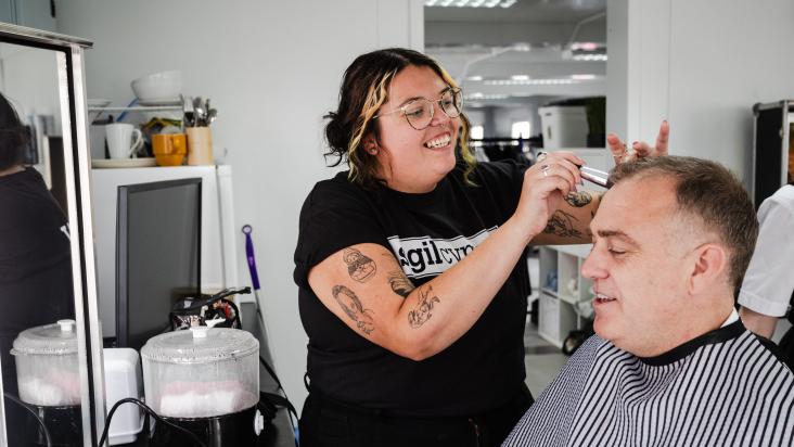 Trainee Fiorella Wyn, smiles as she is doing make up on a male participant back stage