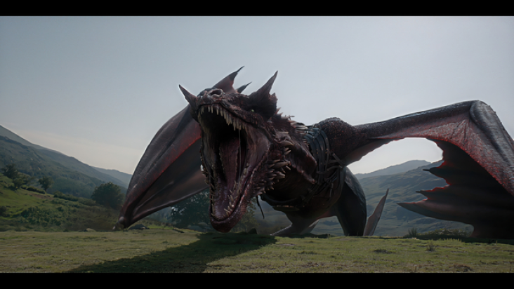 A fierce dragon with outstretched wings roaring on a grassy hillside against a backdrop of mountains and a clear sky